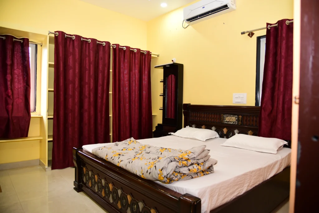 a room is showing a bed with some pilow and a blanket. Room is having some racks and curtains.