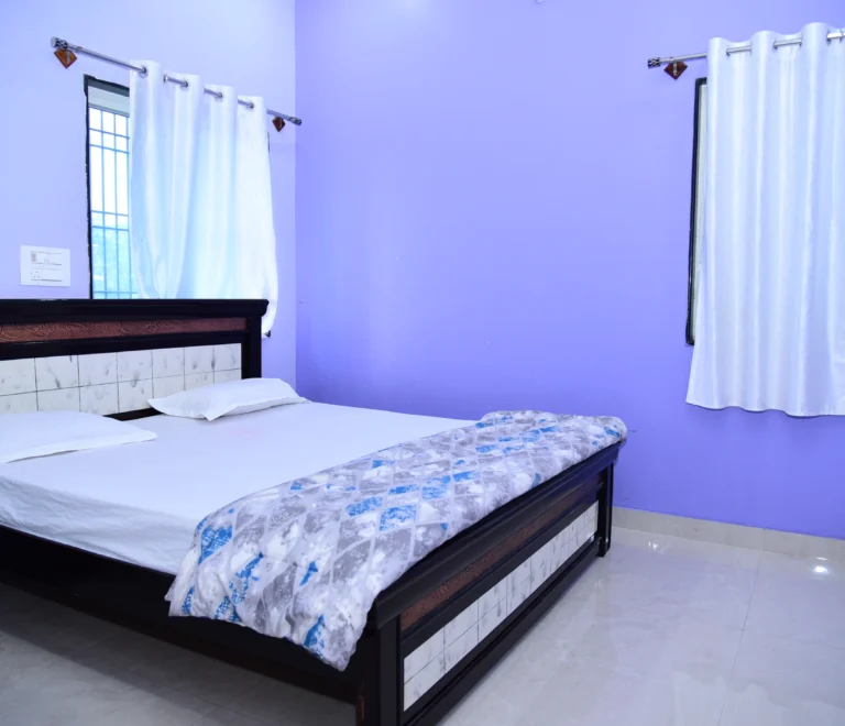 The room features a large double bed with white linens and a patterned throw blanket.